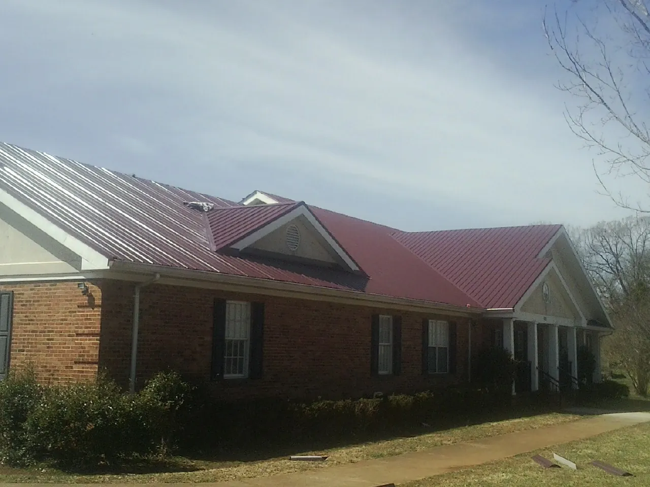 Red metal roof with gabled entries on a long brick building, from a Hail Damage Roof Repair job in Murrysville