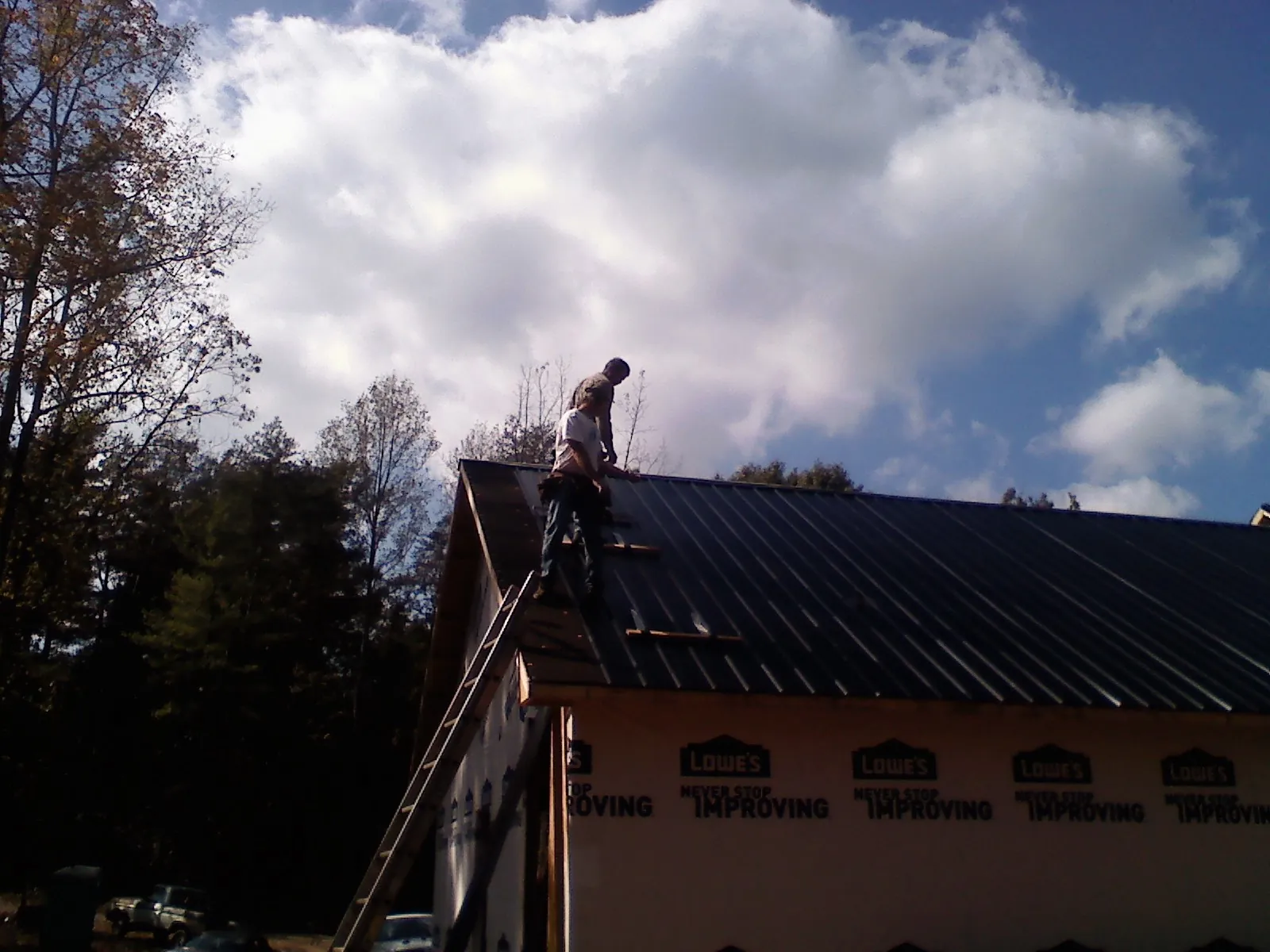Roofer fastening dark metal panels high against a cloudy sky, from a Roof Inspection job in Murrysville