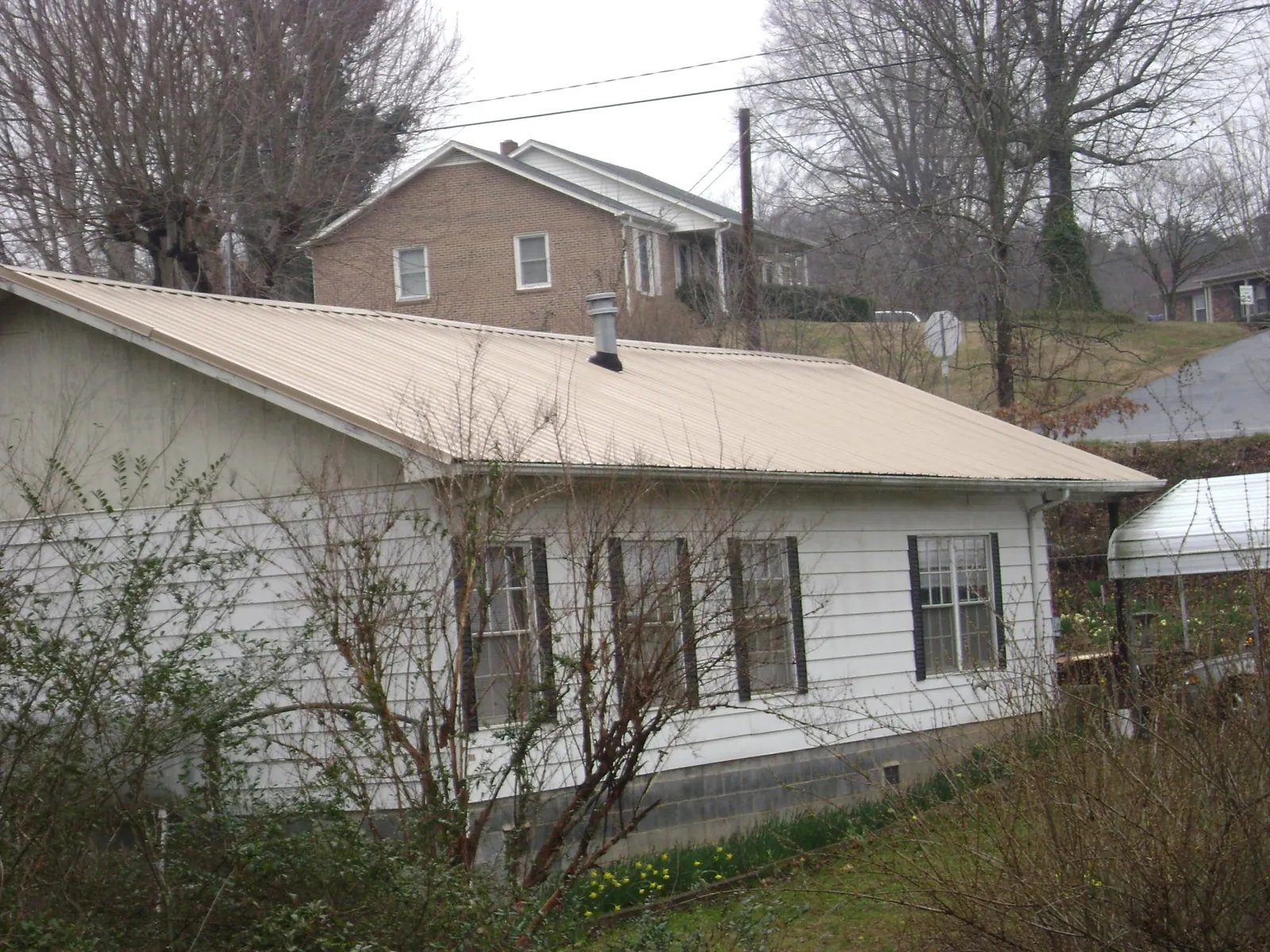 Tan metal roof on a white sided house set into a hillside — Commercial Roofing by Roofing Brothers in Murrysville